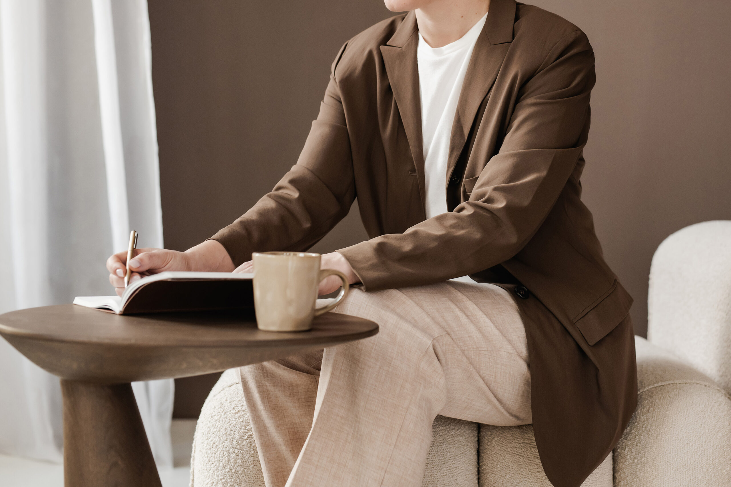 Person at table writing in journal with a mug on table